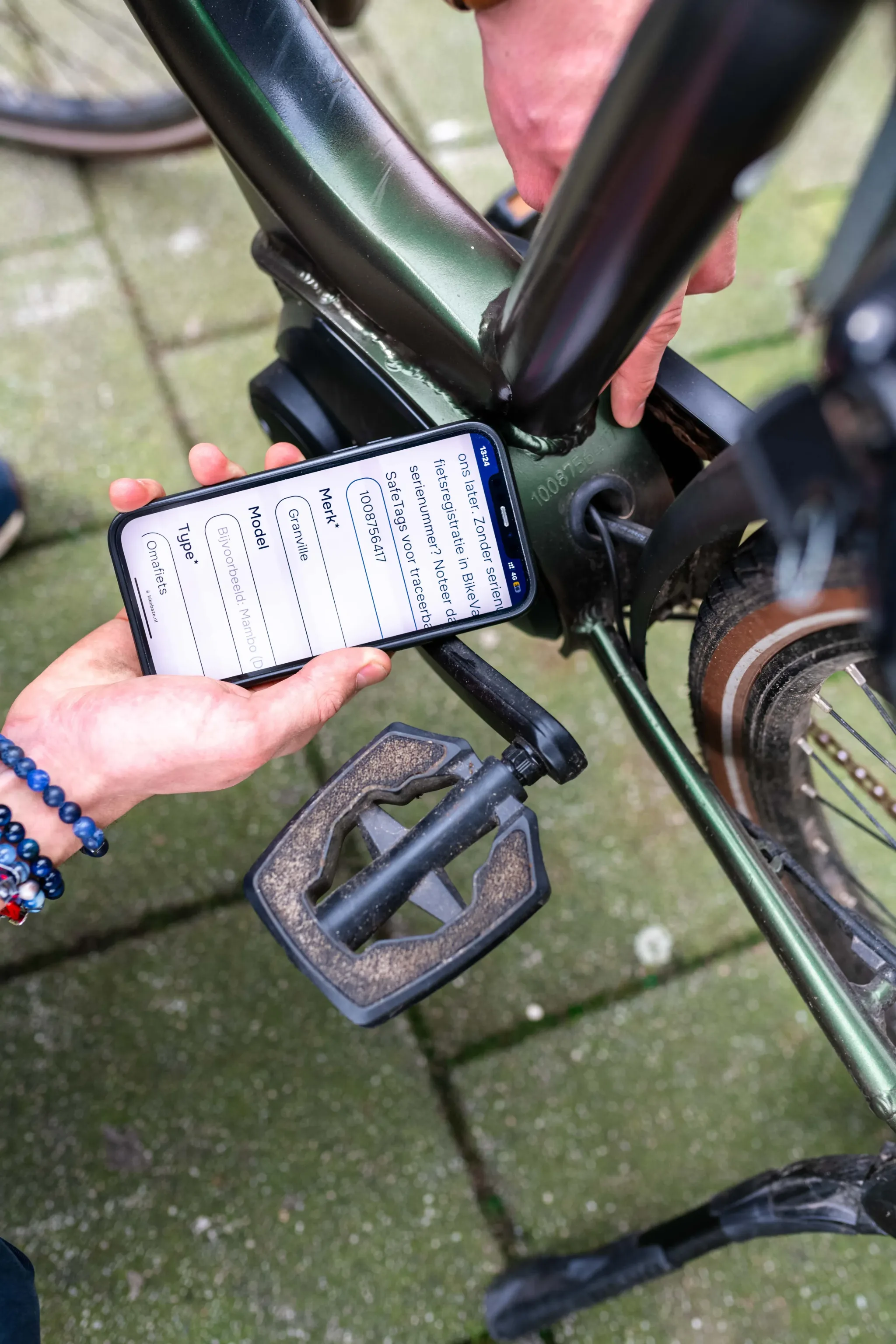 Iemand controleert een framenummer op een groene fiets terwijl een ander de gegevens invoert op een smartphone.