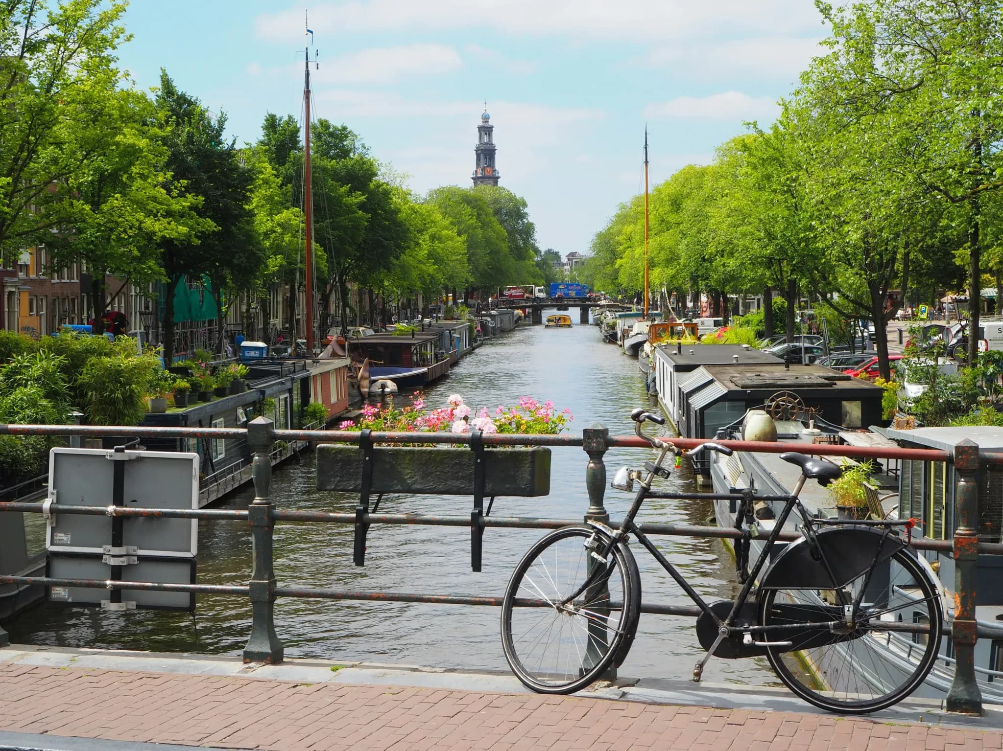 Fiets geparkeerd op Amsterdamse grachtenbrug met woonboten en Westertoren op de achtergrond.