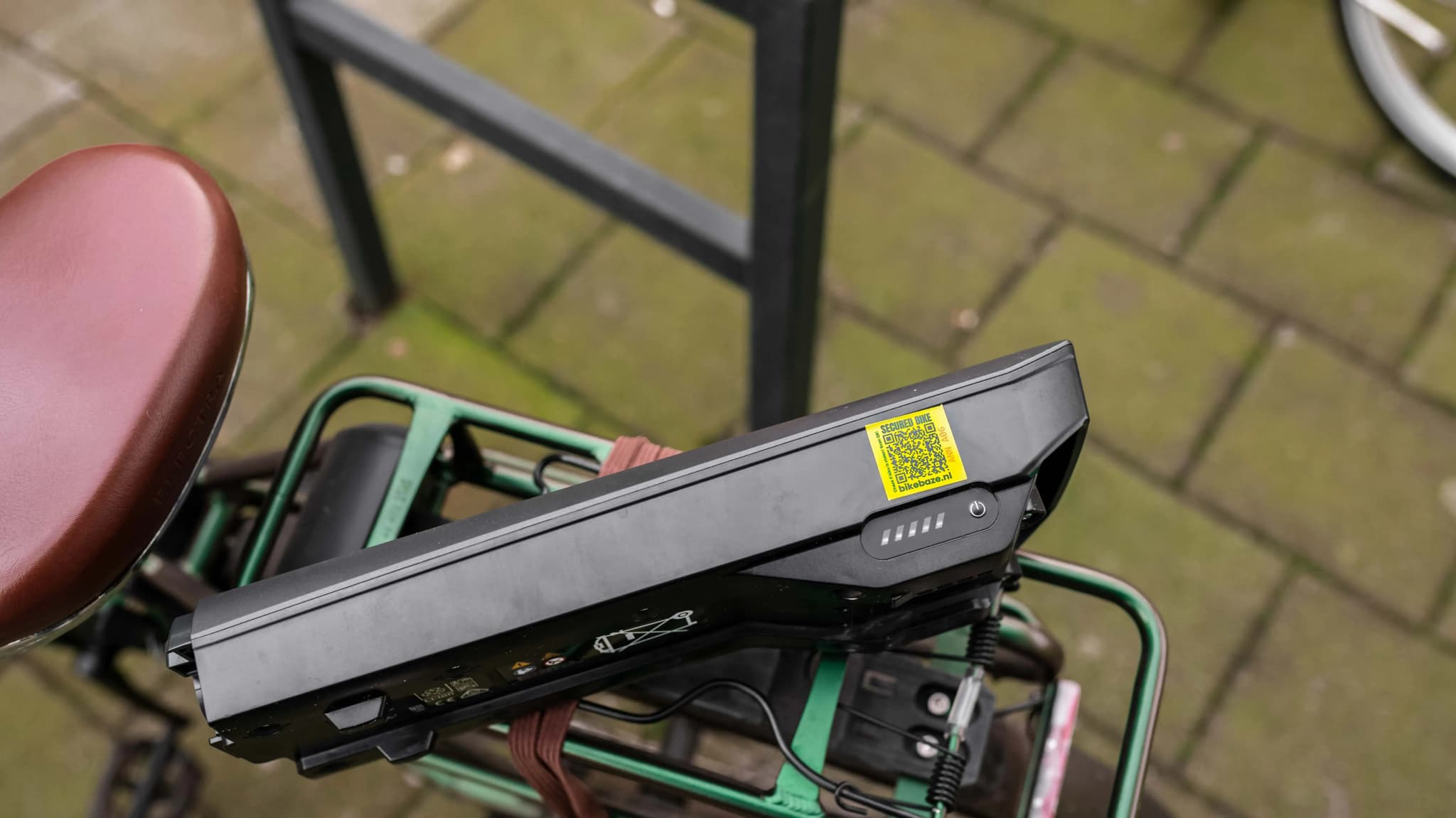 Bovenaanzicht van een zwarte e-bike accu met gele BIKEBAZE QR-sticker, gemonteerd op een groene bakfiets.