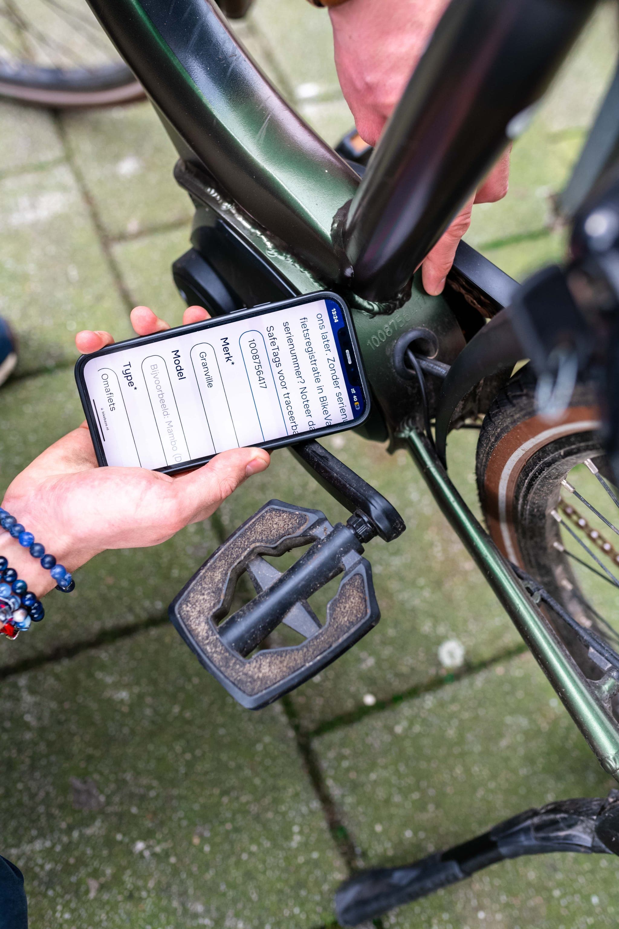 Hands scanning the frame number of a green bike using the BIKEBAZE app on a smartphone.