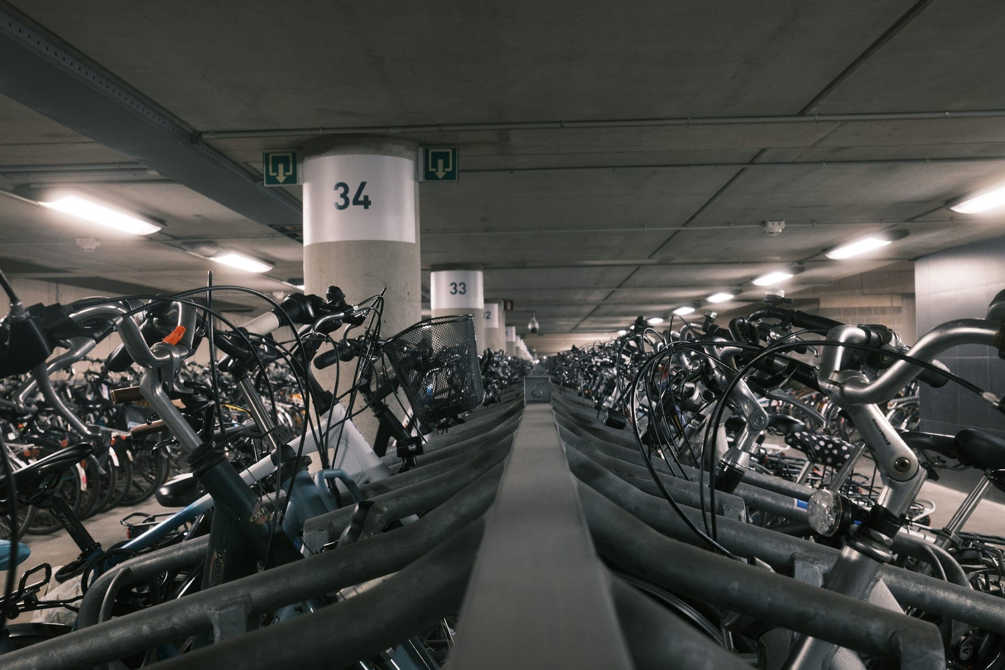 Parking à vélos souterrain sécurisé avec piliers en béton numérotés et des centaines de vélos dans des arceaux métalliques.