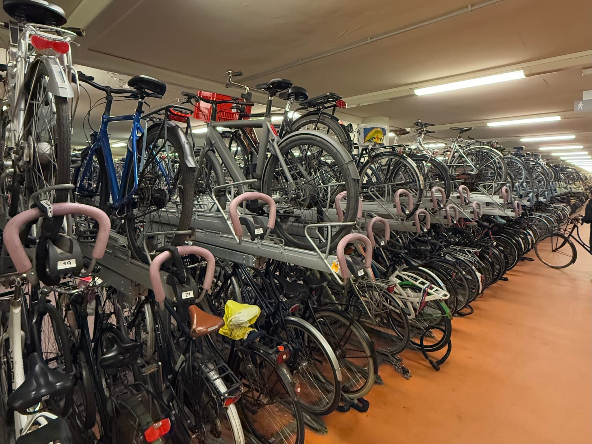 Longue rangée de vélos garés dans des arceaux à deux étages dans un parking à vélos souterrain à un nœud de transport.